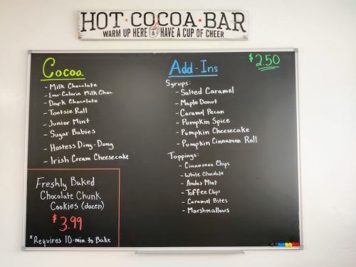 A chalkboard menu for a hot cocoa bar, listing cocoa options, add-ins, and toppings with prices.