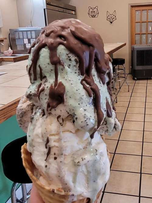 A large ice cream cone with chocolate, mint, and vanilla flavors, held in a hand, inside a cozy ice cream shop.