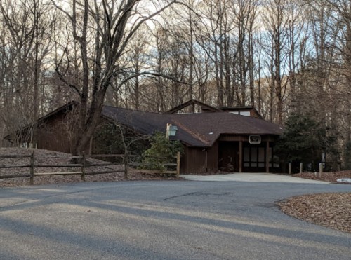 A rustic building surrounded by trees, with a gravel driveway leading up to it.
