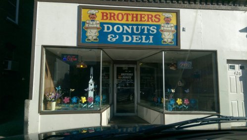 A storefront for "Brothers Donuts & Deli" featuring colorful decorations in the windows and a bright sign.