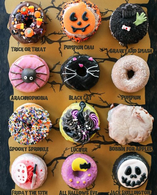 A colorful assortment of themed donuts, including Halloween designs like pumpkins, spiders, and ghosts on a dark background.