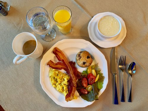 A breakfast plate with scrambled eggs, bacon, salad, a muffin, and drinks including coffee, water, and orange juice.