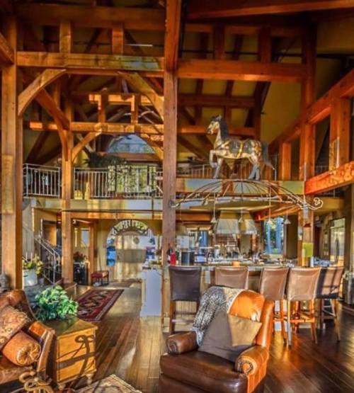A spacious, rustic interior with wooden beams, cozy seating, and a dining area, featuring a horse sculpture above.