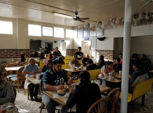 A busy dining area with people eating at tables, surrounded by brick walls and vintage photos.