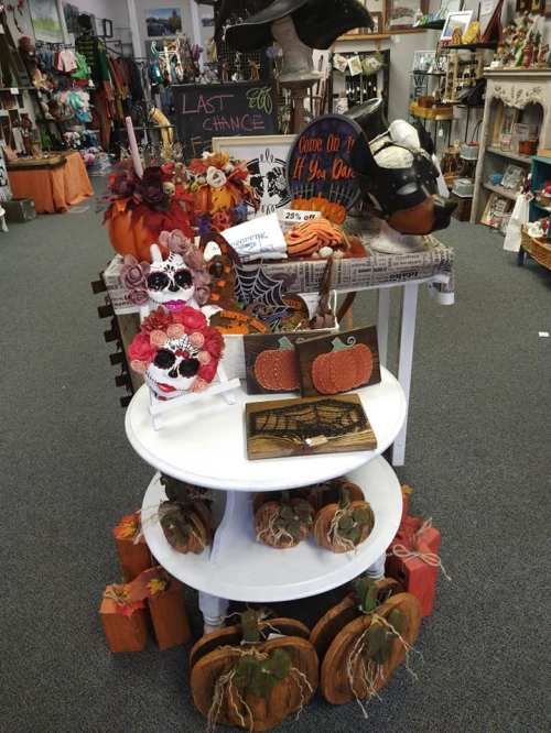 A display of Halloween decorations, including pumpkins, skulls, and festive signs, in a cozy shop setting.