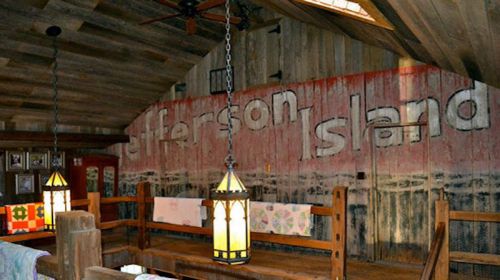 Interior of a rustic room with wooden walls, featuring the words "Jefferson Island" and hanging lanterns.