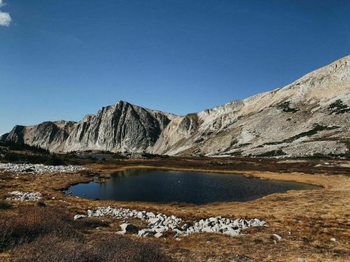 A serene landscape featuring mountains, a calm pond, and grassy terrain under a clear blue sky.