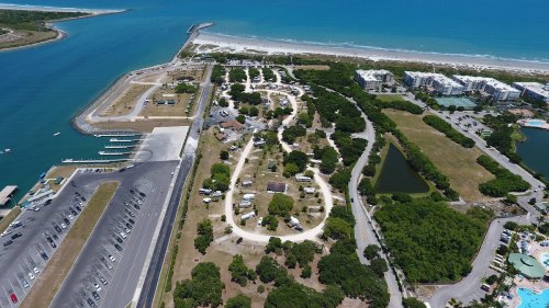 Aerial view of a coastal area featuring a campground, parking lot, and nearby beach with clear blue water.