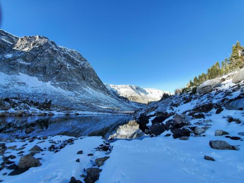 A serene winter landscape featuring snow-covered mountains and a calm lake reflecting the clear blue sky.