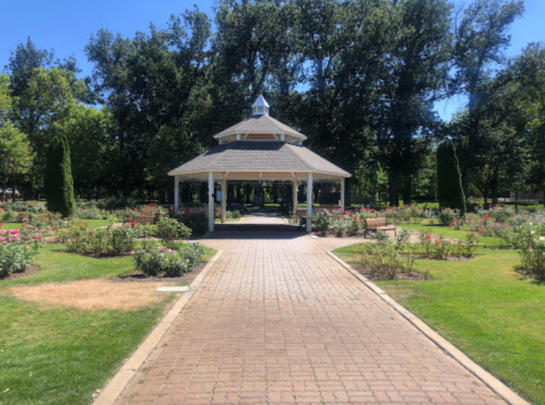 A pathway leads to a gazebo surrounded by lush gardens and trees under a clear blue sky.