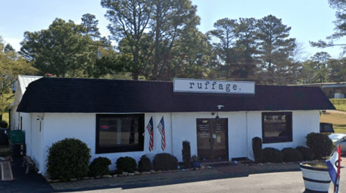 A white building with a black roof, featuring the sign "ruffage" and American flags outside. Surrounded by greenery.