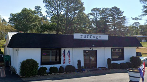 A white building with a black roof, featuring the sign "ruffage" and American flags outside. Surrounded by greenery.