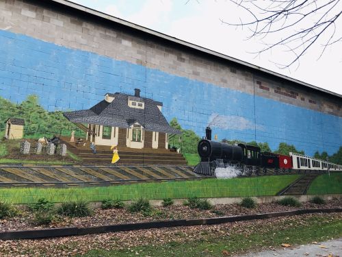 A colorful mural depicting a vintage steam train and a house with a person in a yellow dress on a train platform.