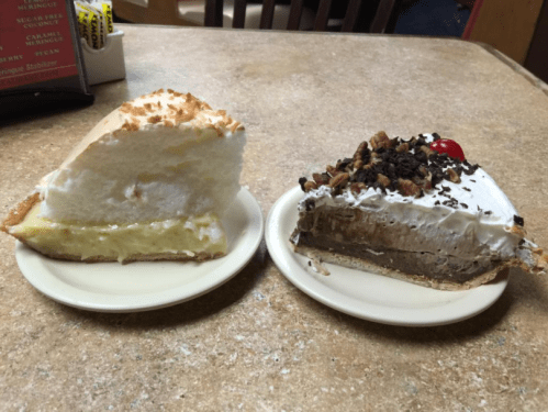 Two slices of pie on plates: one lemon meringue with fluffy topping, the other chocolate with whipped cream and a cherry.