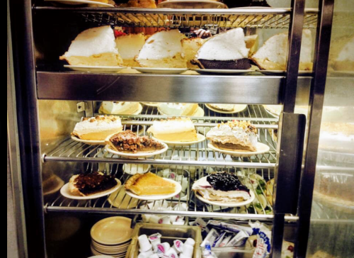 A display case filled with various pies on plates, showcasing different flavors and toppings.