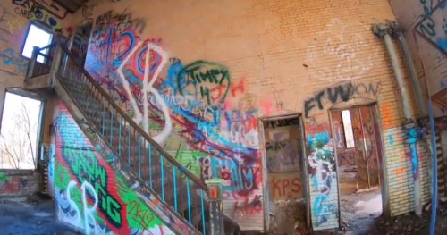Interior of an abandoned building with colorful graffiti on the walls and a staircase leading to the upper floor.