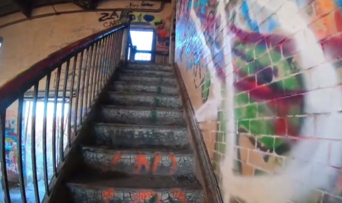 A worn staircase leads upward, surrounded by colorful graffiti on the walls and steps. Natural light filters in from above.