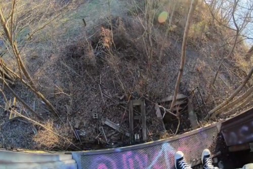 A view from above showing a wooded area with debris and graffiti on the ground below.