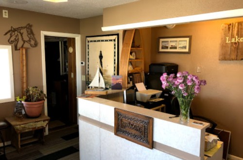 A cozy reception area with a desk, flowers, and rustic decor, featuring a horse silhouette and lake-themed artwork.