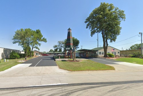 A colorful tower stands in front of a building complex with trees and a clear blue sky.