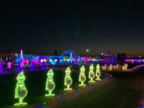 Colorful holiday lights illuminate a festive scene with glowing Grinch figures against a night sky.