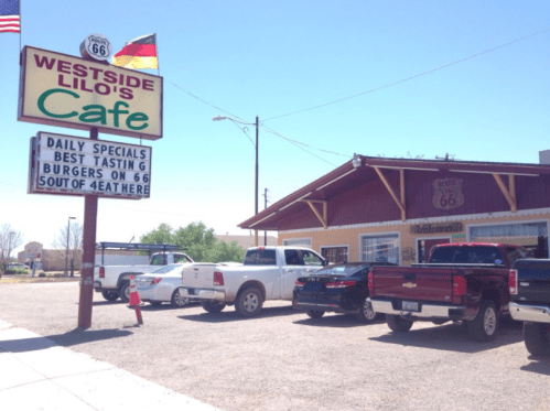 Sign for Westside Lilo's Cafe with daily specials, burgers, and Route 66 theme; cars parked outside in a sunny setting.