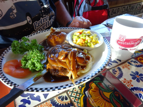 A plate of meat with gravy, a side of mixed vegetables, a tomato slice, and a coffee mug on a colorful table.