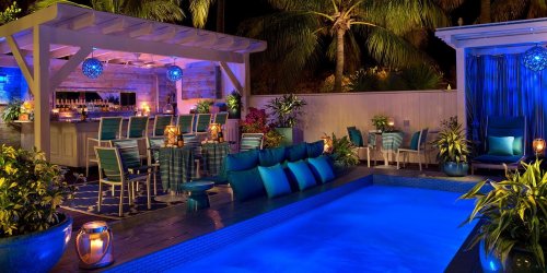 A beautifully lit outdoor lounge area with a pool, bar, and tropical plants, creating a relaxing evening atmosphere.