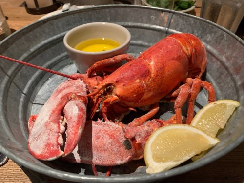 A cooked lobster in a metal bowl, accompanied by a small dish of melted butter and lemon wedges.