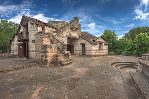 Historic stone building with a unique architectural design, surrounded by greenery and under a blue sky.