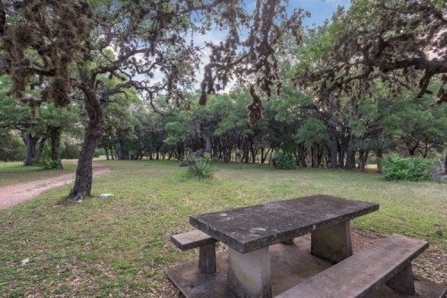 A stone picnic table surrounded by lush greenery and trees in a peaceful park setting.