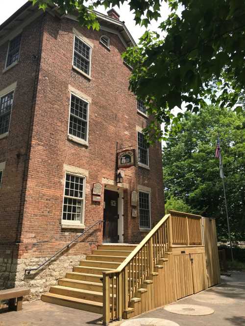 Historic brick building with large windows, a wooden staircase, and greenery surrounding it.