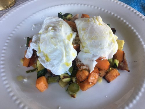 A plate of poached eggs atop a colorful vegetable medley, including sweet potatoes and zucchini, drizzled with olive oil.