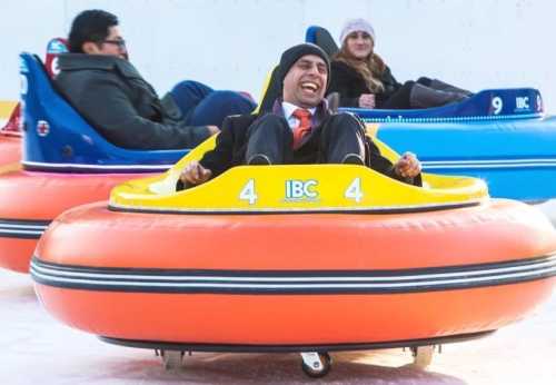 A man in a suit joyfully rides a bumper car, with two others in the background enjoying the amusement.