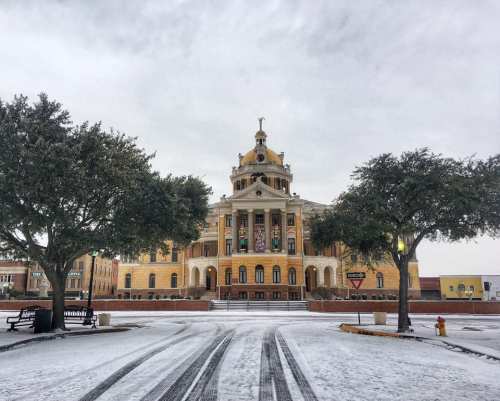 Historic building with a dome, surrounded by snow-covered trees and a quiet street in winter.