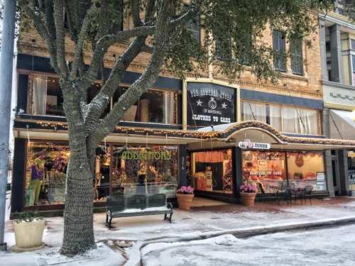 A charming storefront decorated with lights, surrounded by snow and a tree, showcasing clothing and accessories.