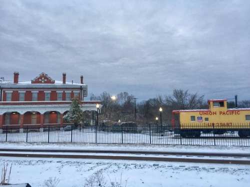 A snowy scene featuring a historic train station and a yellow Union Pacific train car beside the tracks.
