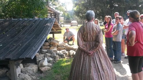 A group of people watches a demonstration outdoors, with one person in historical clothing standing in the foreground.