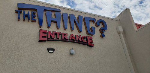 Sign on a building reading "THE THING? ENTRANCE" against a cloudy sky.