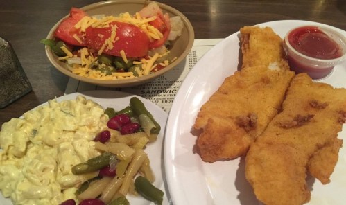 A plate with fried fish, a side of salad with cheese, and a bowl of mixed vegetables and pasta.