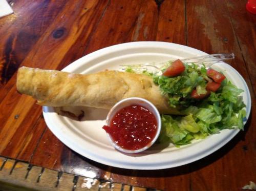 A plate with a large rolled tortilla filled with ingredients, accompanied by lettuce, diced tomatoes, and a small cup of salsa.