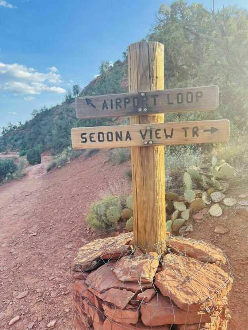 Wooden signpost with directional arrows for "Airport Loop" and "Sedona View Trail" on a rocky path in a desert landscape.