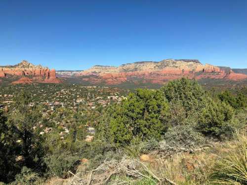 A panoramic view of red rock formations and green vegetation under a clear blue sky in Sedona, Arizona.