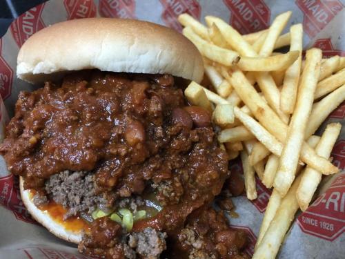 A hearty burger topped with chili and served with a side of golden fries in a red and white basket.