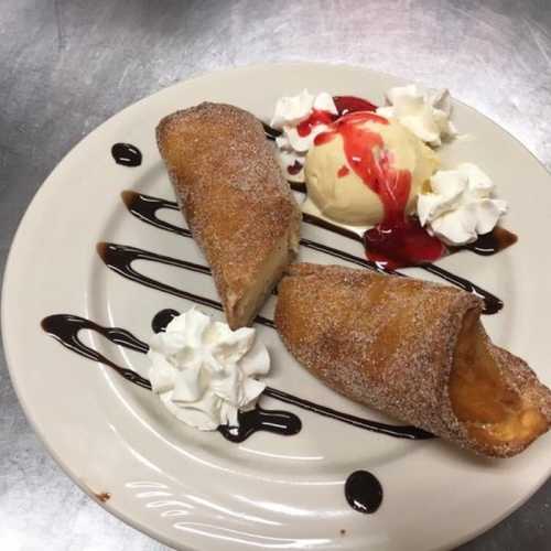 Two cinnamon-sugar dusted pastries with a scoop of ice cream, whipped cream, and chocolate sauce on a plate.