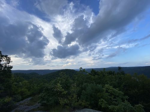 A scenic view of rolling hills under a cloudy sky, with lush greenery in the foreground.