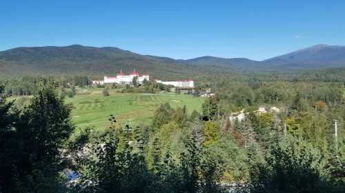 A scenic view of a large hotel surrounded by lush greenery and mountains under a clear blue sky.