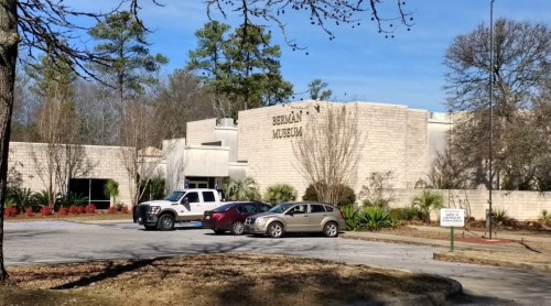 Exterior view of the Berman Museum, featuring a parking lot with several cars and surrounding trees.