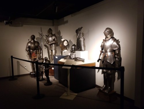 A display of various suits of medieval armor in a museum setting, illuminated by soft lighting.