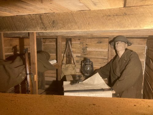 A soldier mannequin sits at a table in a wooden bunker, with a lantern and maps, evoking a historical military setting.